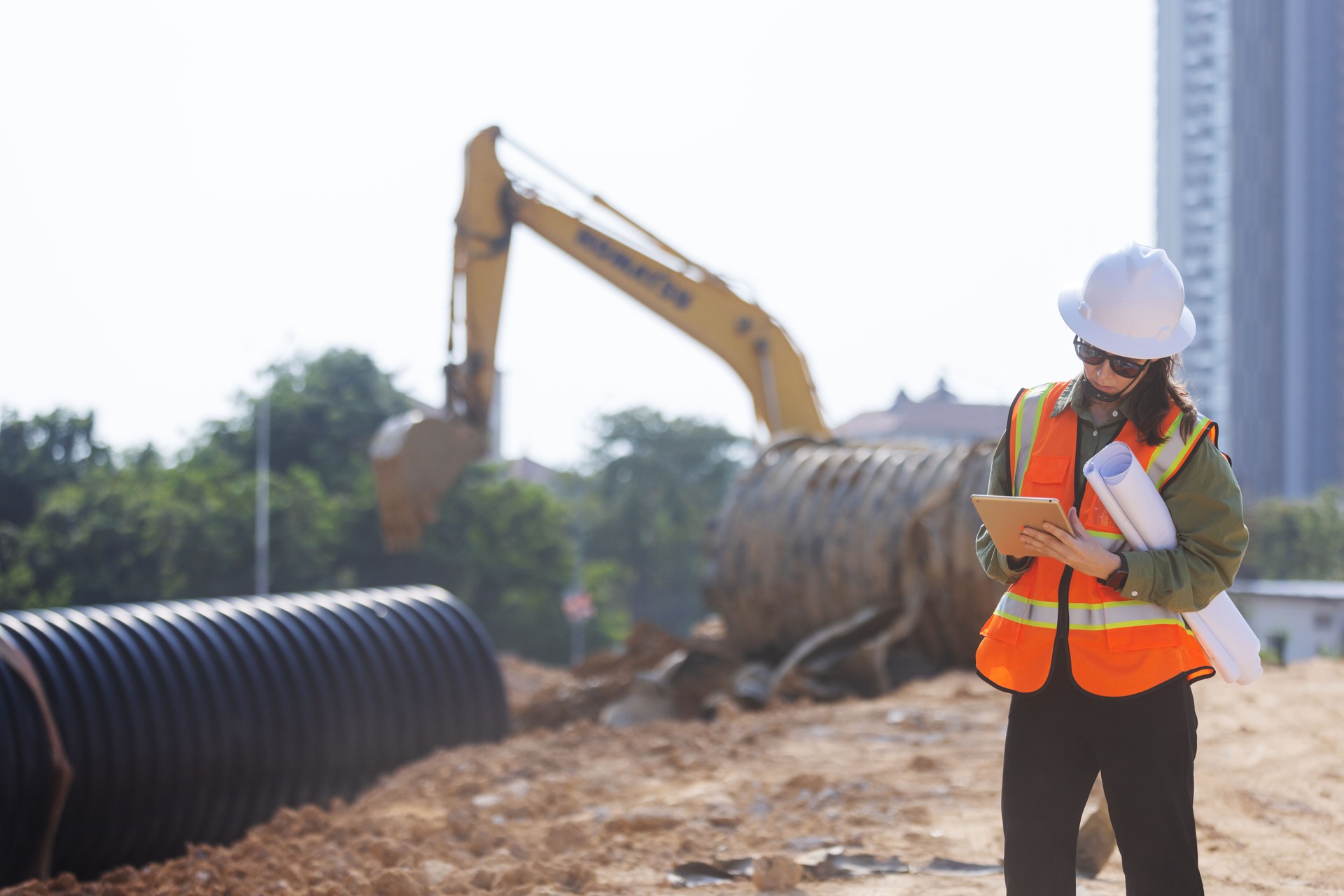 A female engineer  inspects a construction site, taking notes on a tablet.